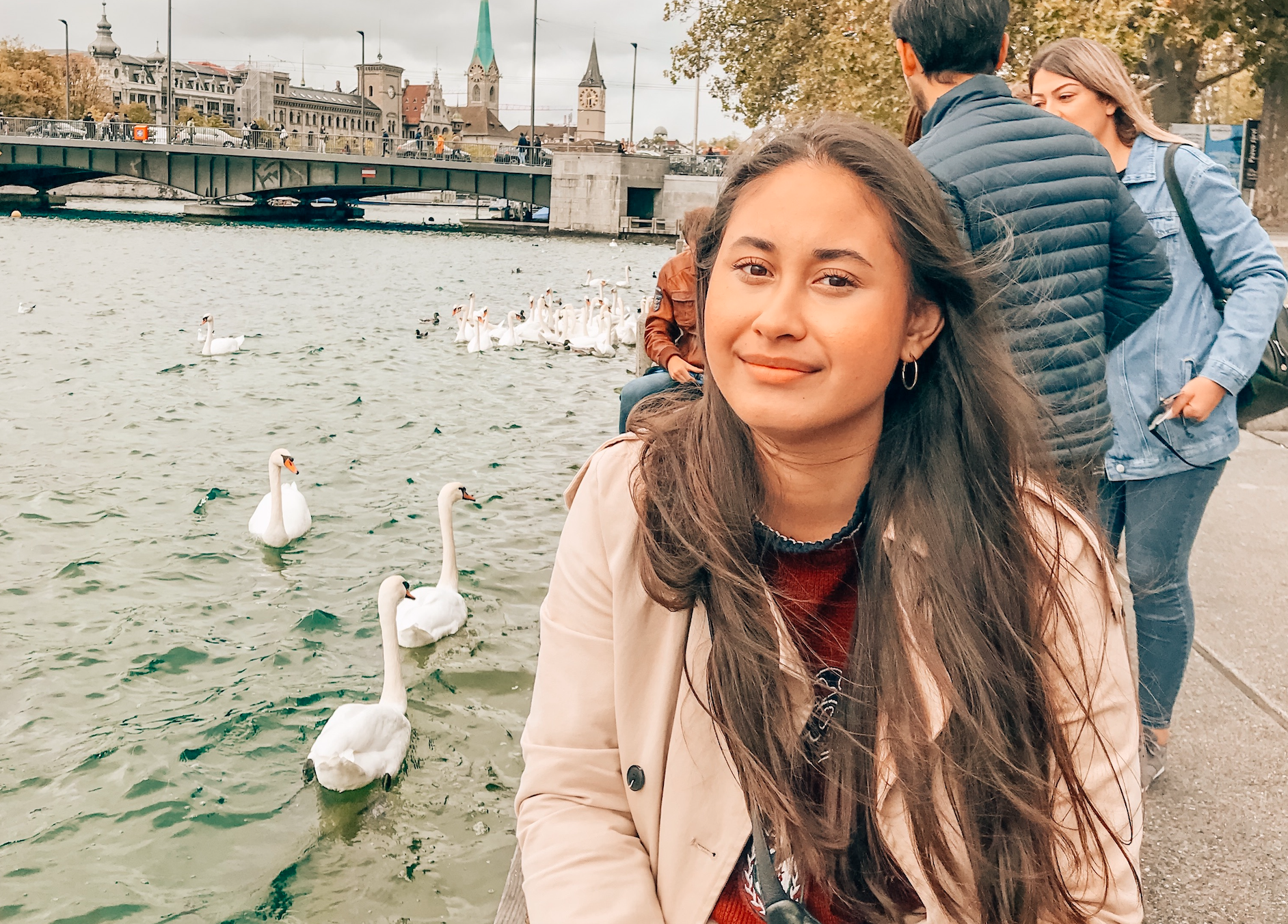 In Switzerland Zurich, a girl who is working for a travel startup during a global pandemic is sitting next to a river with swans