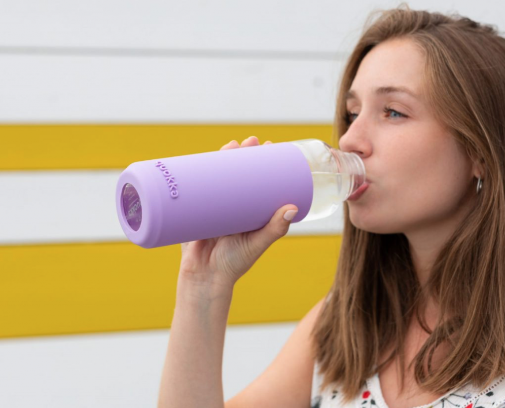 A girl standing in front of a yellow and white striped wall using a cool travel essential, a multifunctional water bottle.