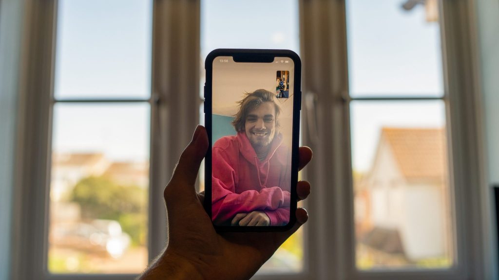 A person holding up a cell phone and skyping with a young man.