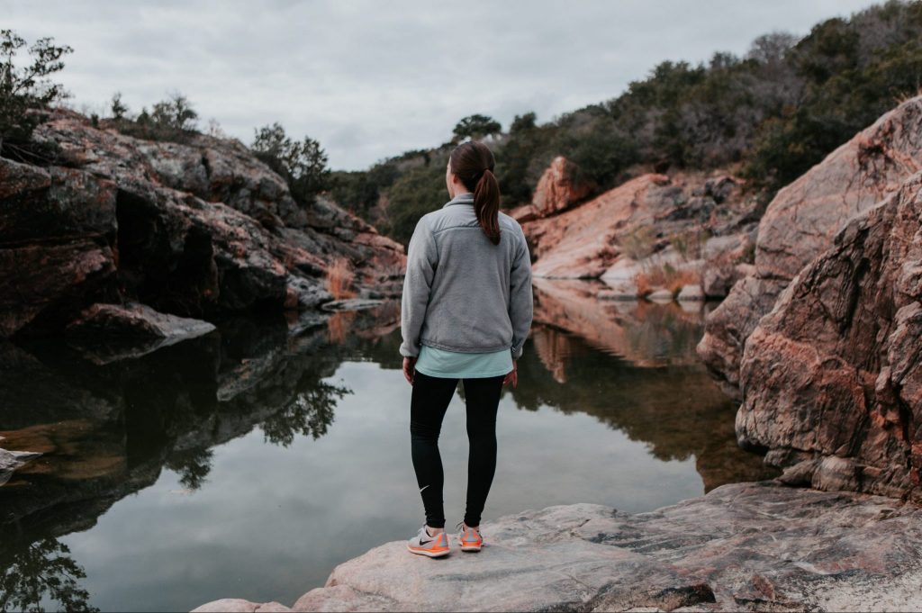 Jacob's Well in Texas, with a woman standing in front of it looking out over the landscape.