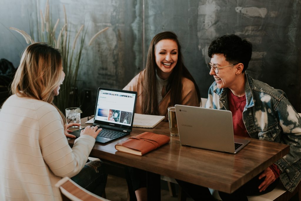 3 woman sitting around a table with their laptops open and they are laughing.