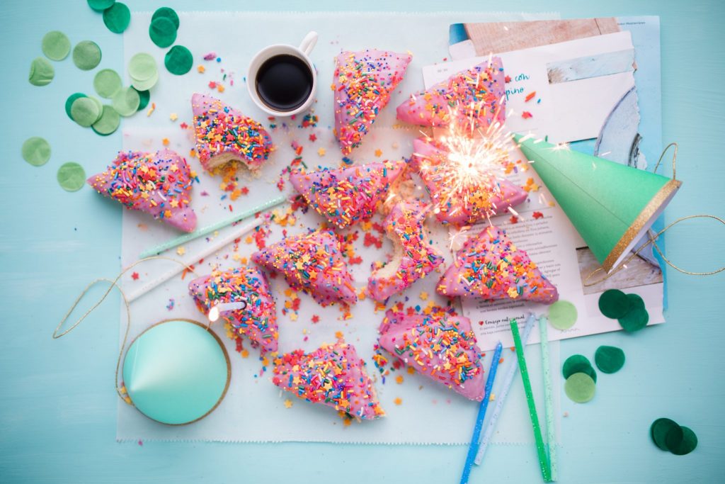 Sweets for all on a baby blue table with confettis and party hats.