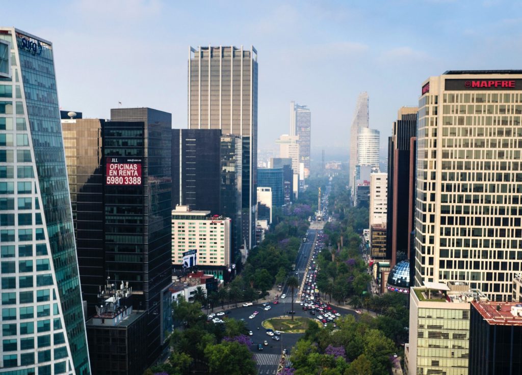 Skyline of Mexico City with tall skyscrapers and green trees lining the roads. 