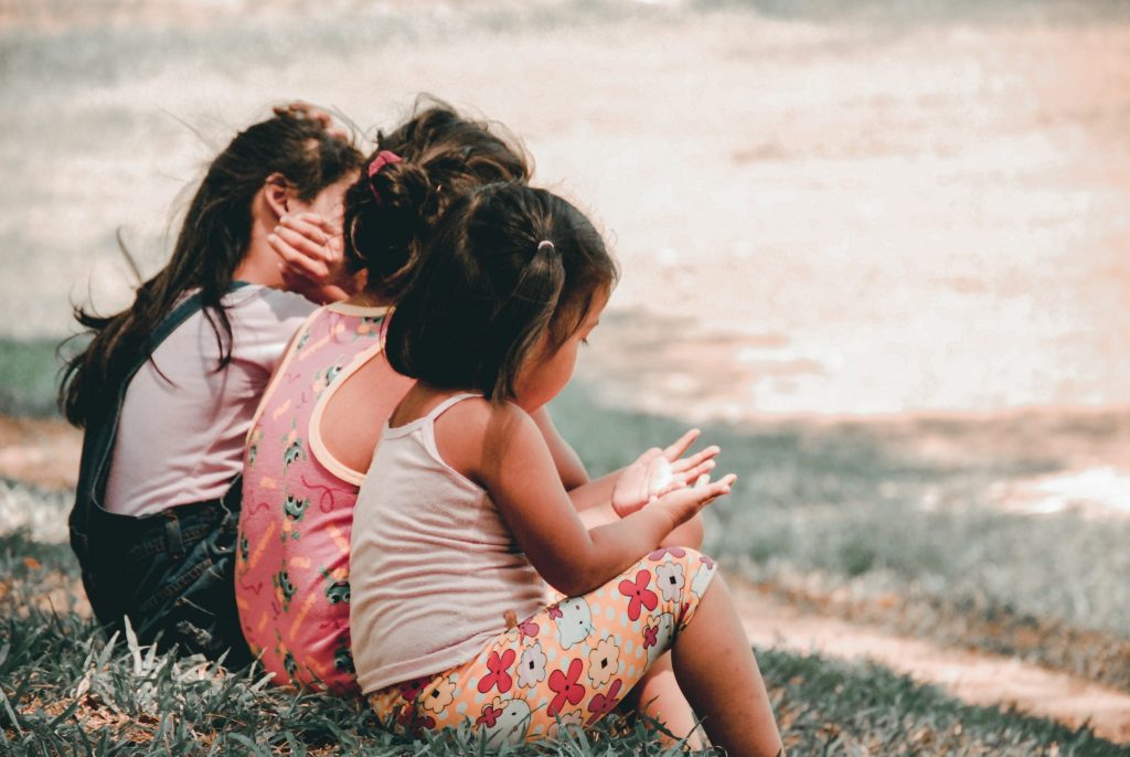 3 girl kids sitting next to each other by the sea.