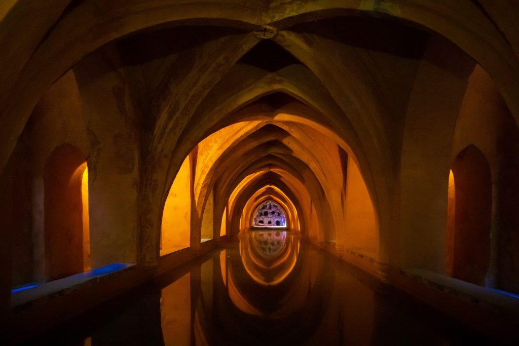 Plan your 2021 travel to Spain, El Real Alcázar de Sevilla where there is. aunique architecture building with warm orange lighting.