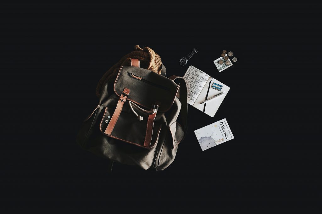 a black bag, notebook, black watch and coins laid out on a black table.