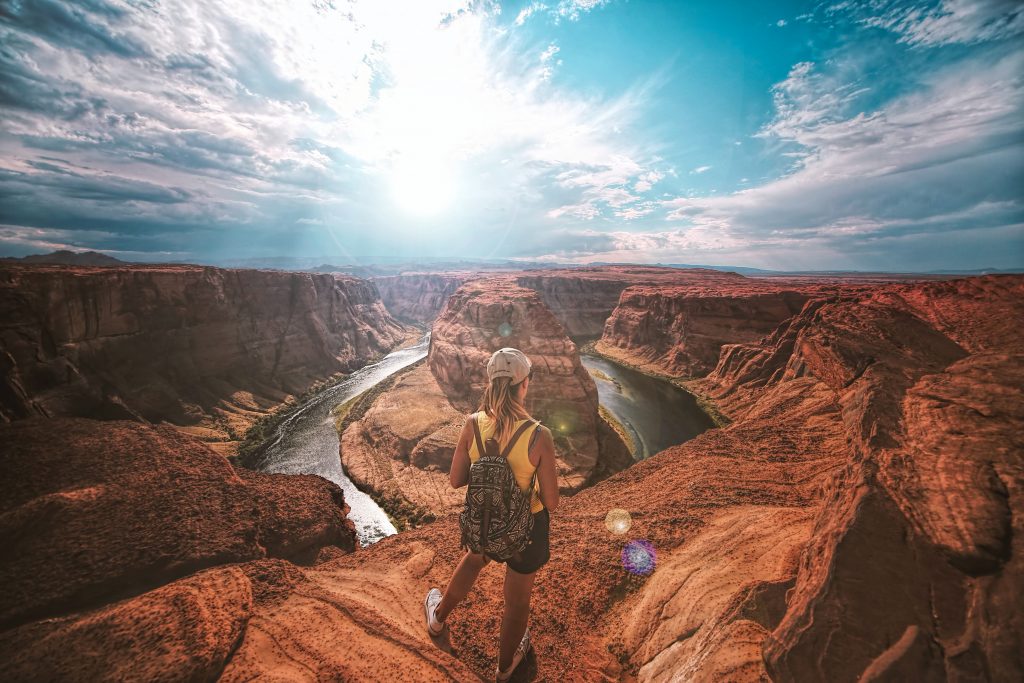 a girl standing on top of huge orange rocks while spectating the view of rock formations infront of her.