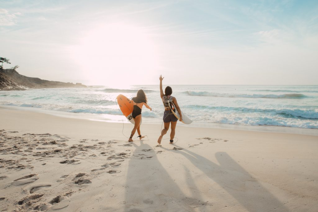 2 girls on the beach walking towards the water with their surfboards.