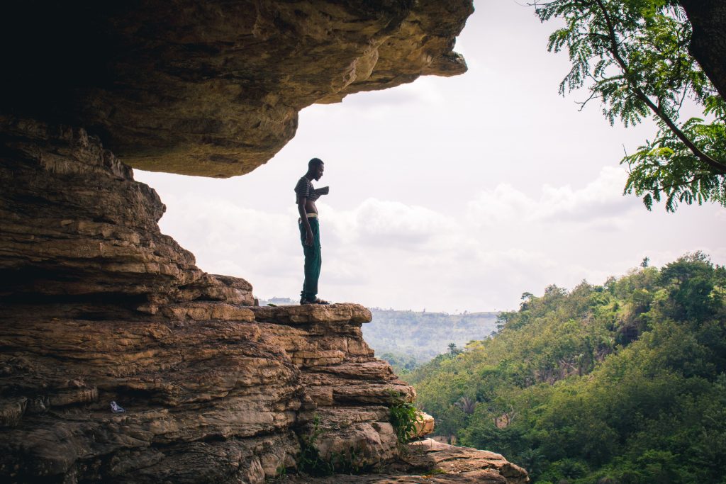 Somewhere in Ghana with a man standing on top of a cliff.