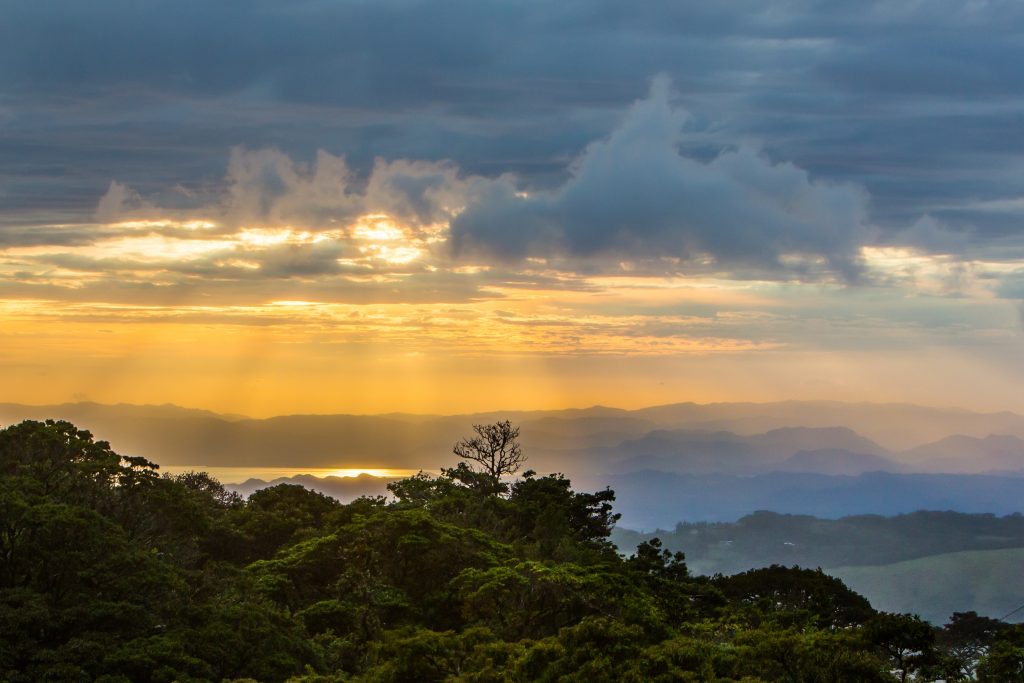 The sun shining through the clouds above a green landscape