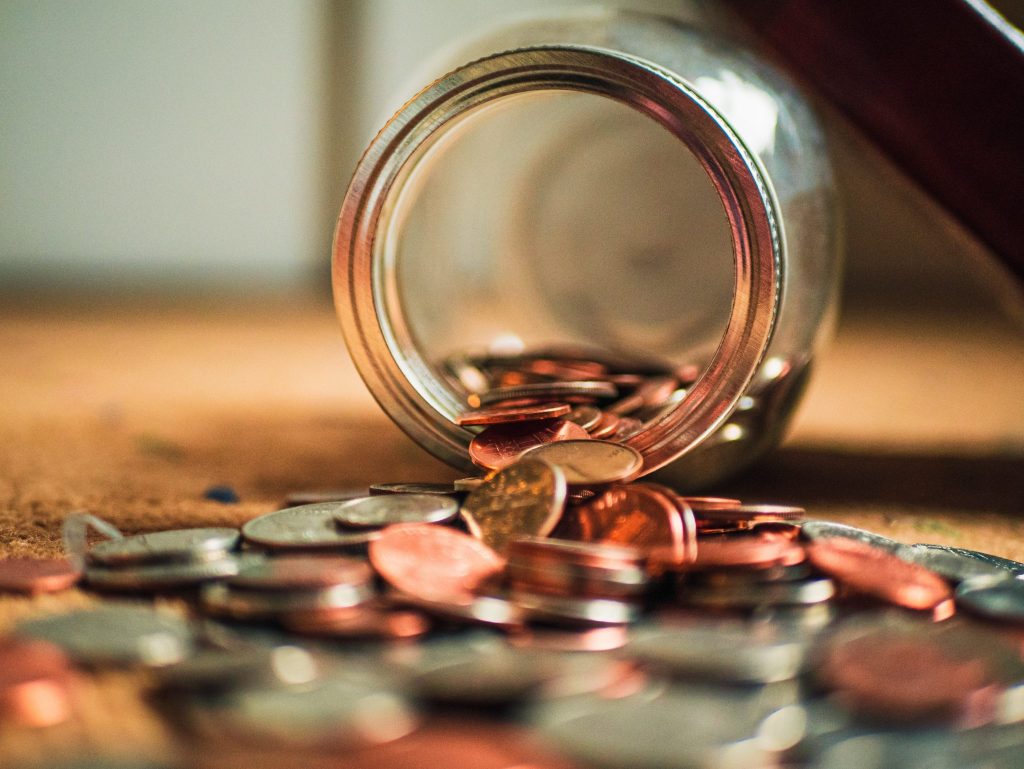 A jar full of money coins that has fallen over.