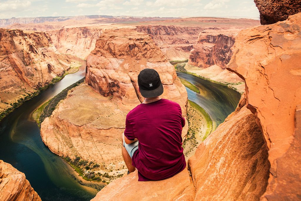 A man in a red shirt and black cap sitting on a brown mountain. 