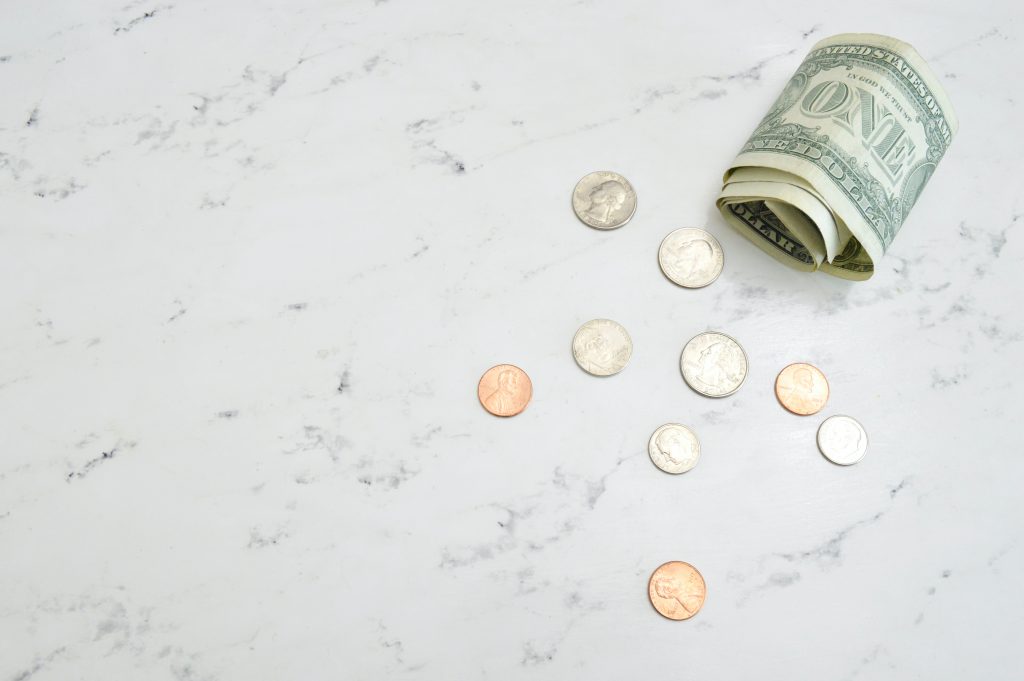 A dollar note and some coins on a marble table.