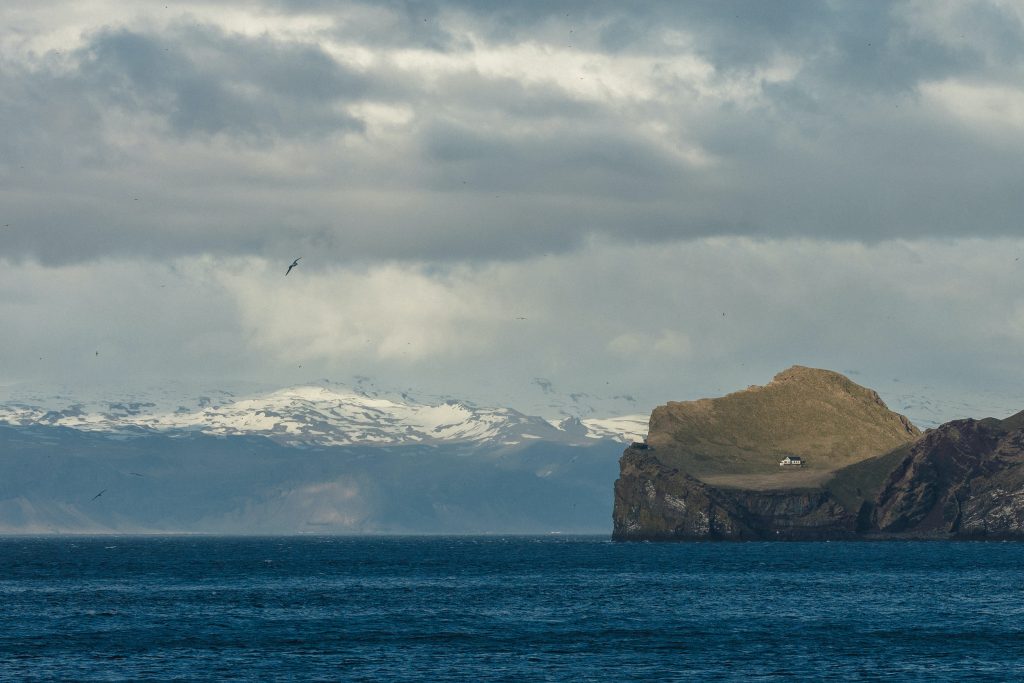 Heimaey island in Iceland with a view of a White House isolated alone on a green island with blue water surrounding it.