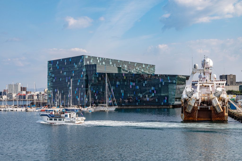 Harpa concert hall in Reykjavik, Iceland by the blue water with boats driving past in the day.