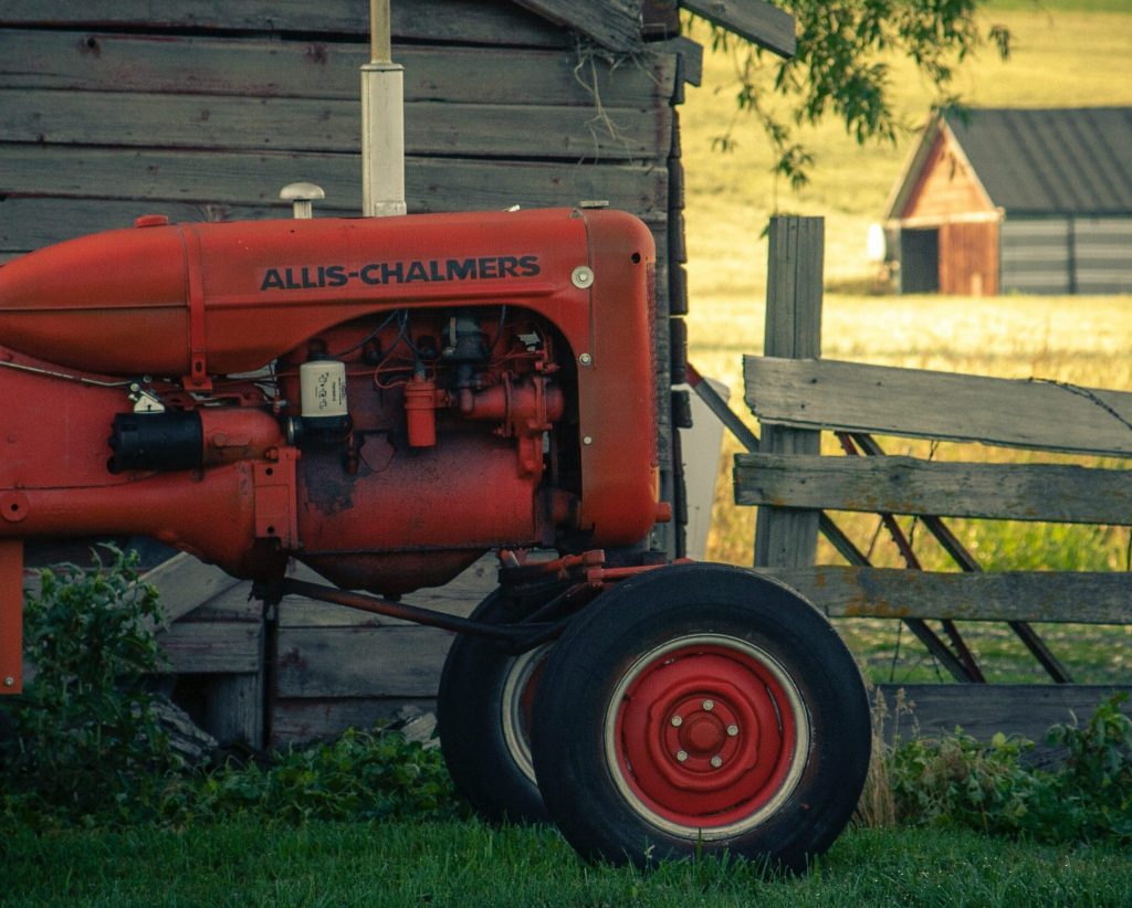 a red truck on a farm with a red farm house in the distance a great way to go abroad.