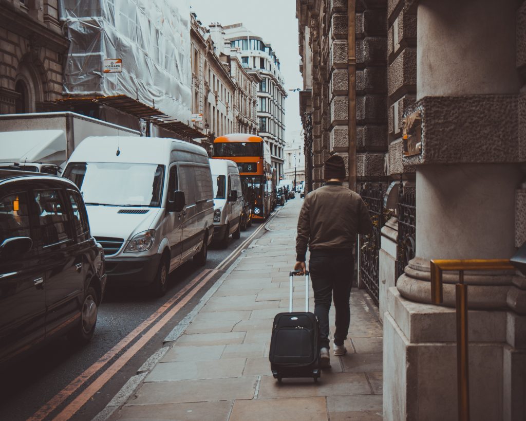 a man walking alone down a street with a black suitcase.