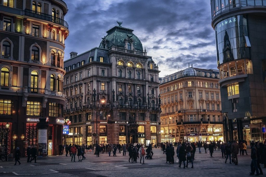 3 buildings in Austria city centre with people walking around shopping.