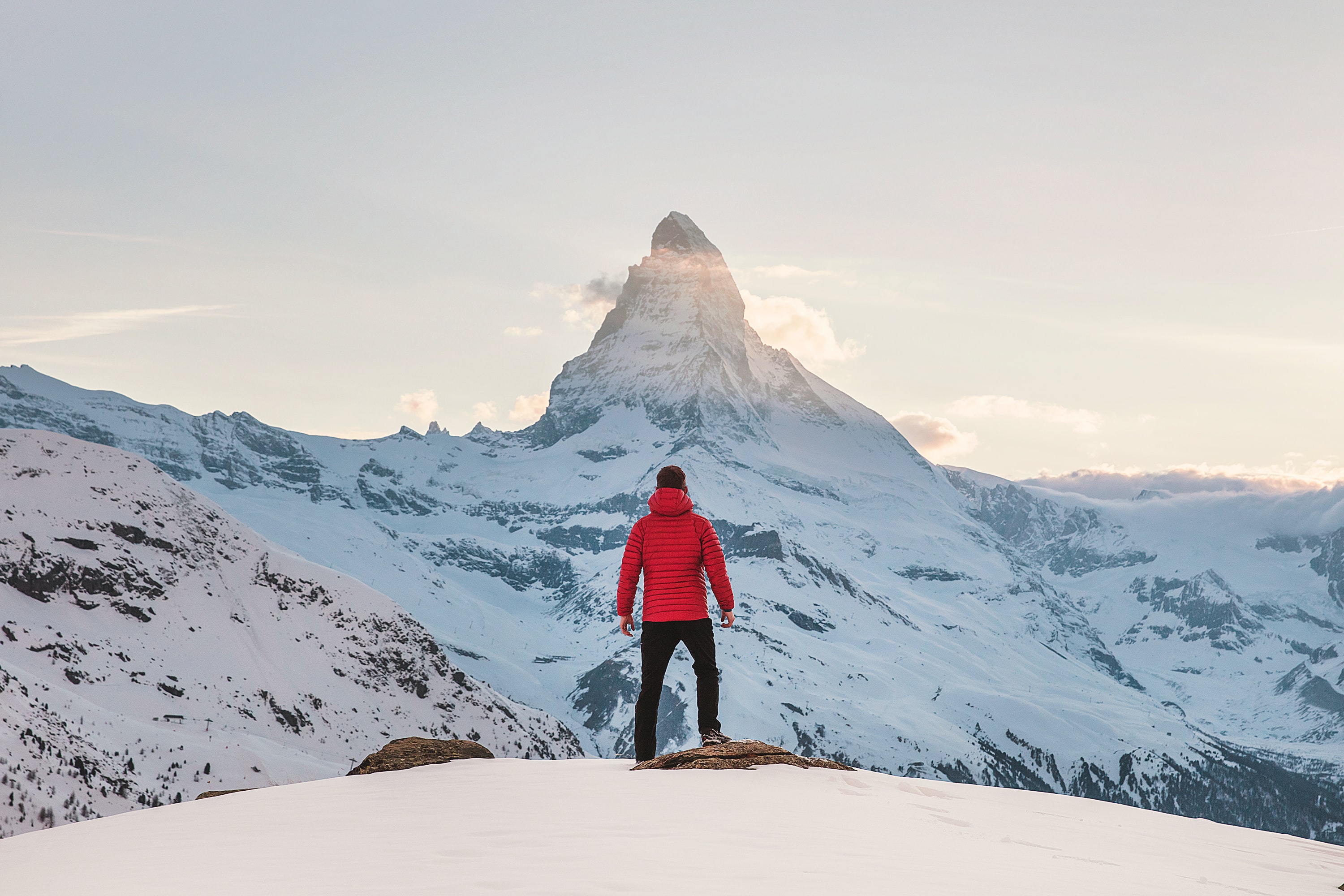 A hiker in red jacket in front of snowy Matterhorn in Zermatt.