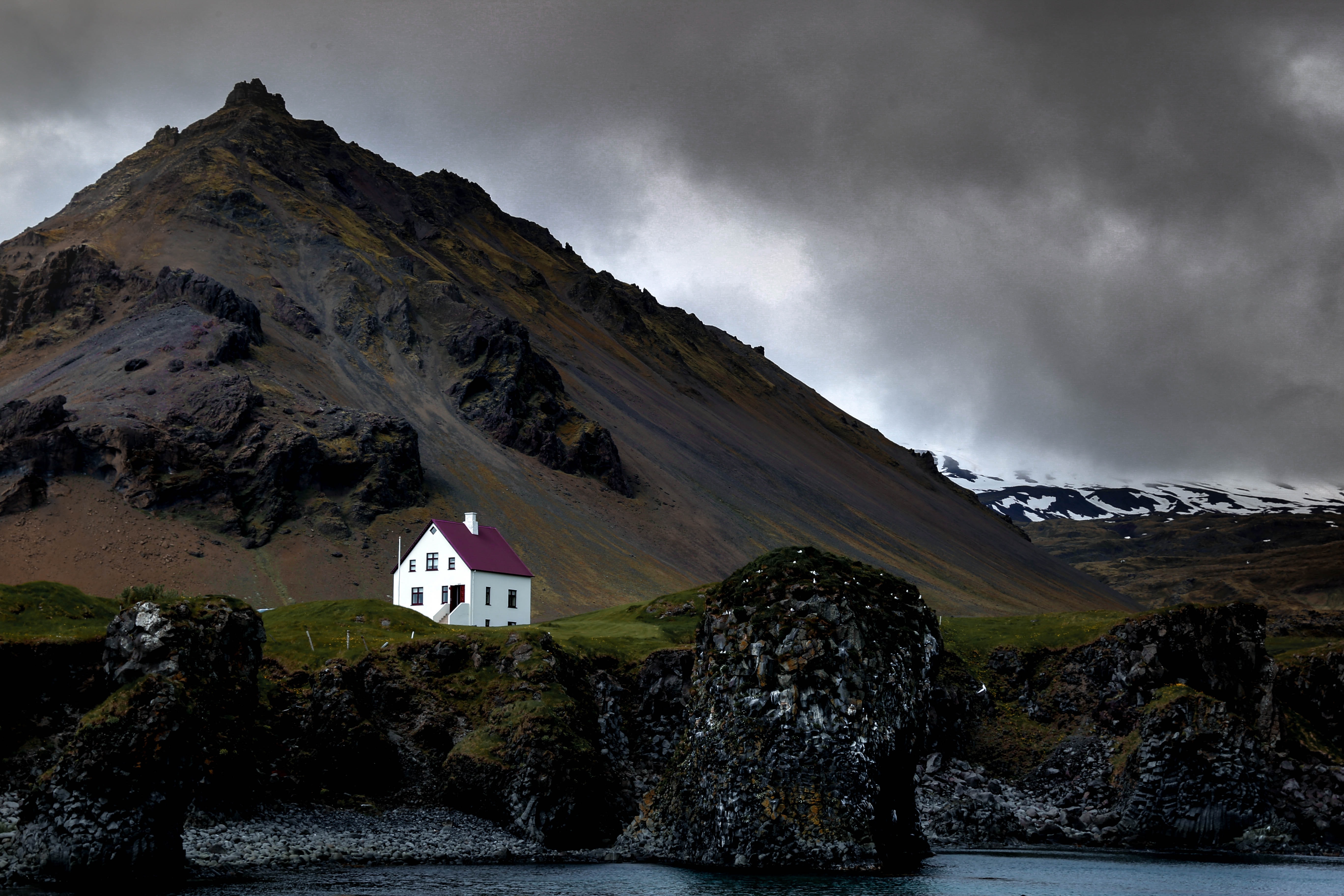 A white house against black moody cliffs in Iceland