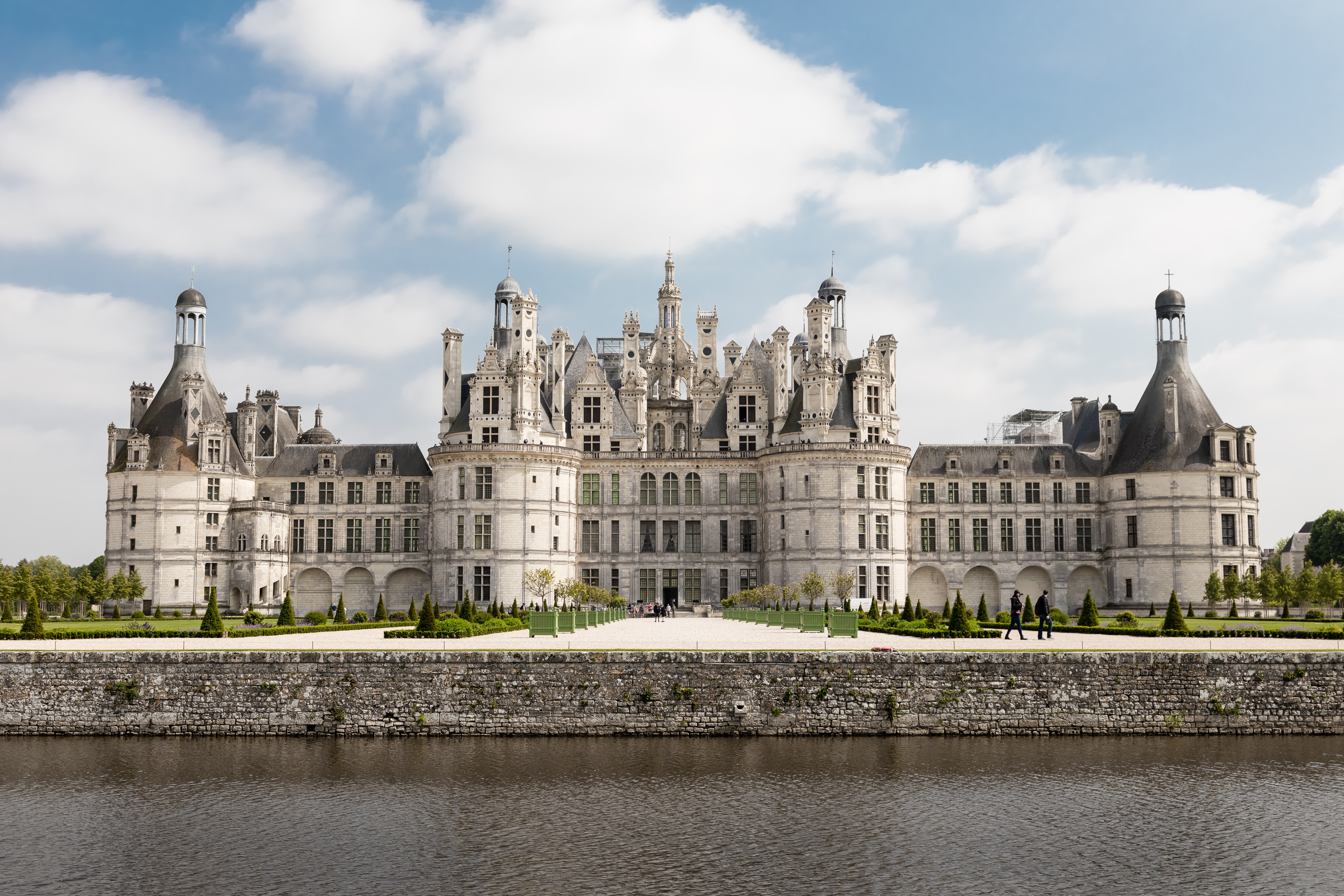 A massive white Renaissance French castle with gardens and water at the front