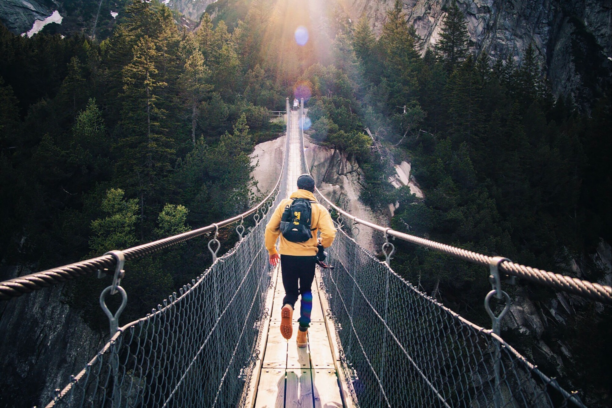 A guy in a yellow jacket running across a bridge.