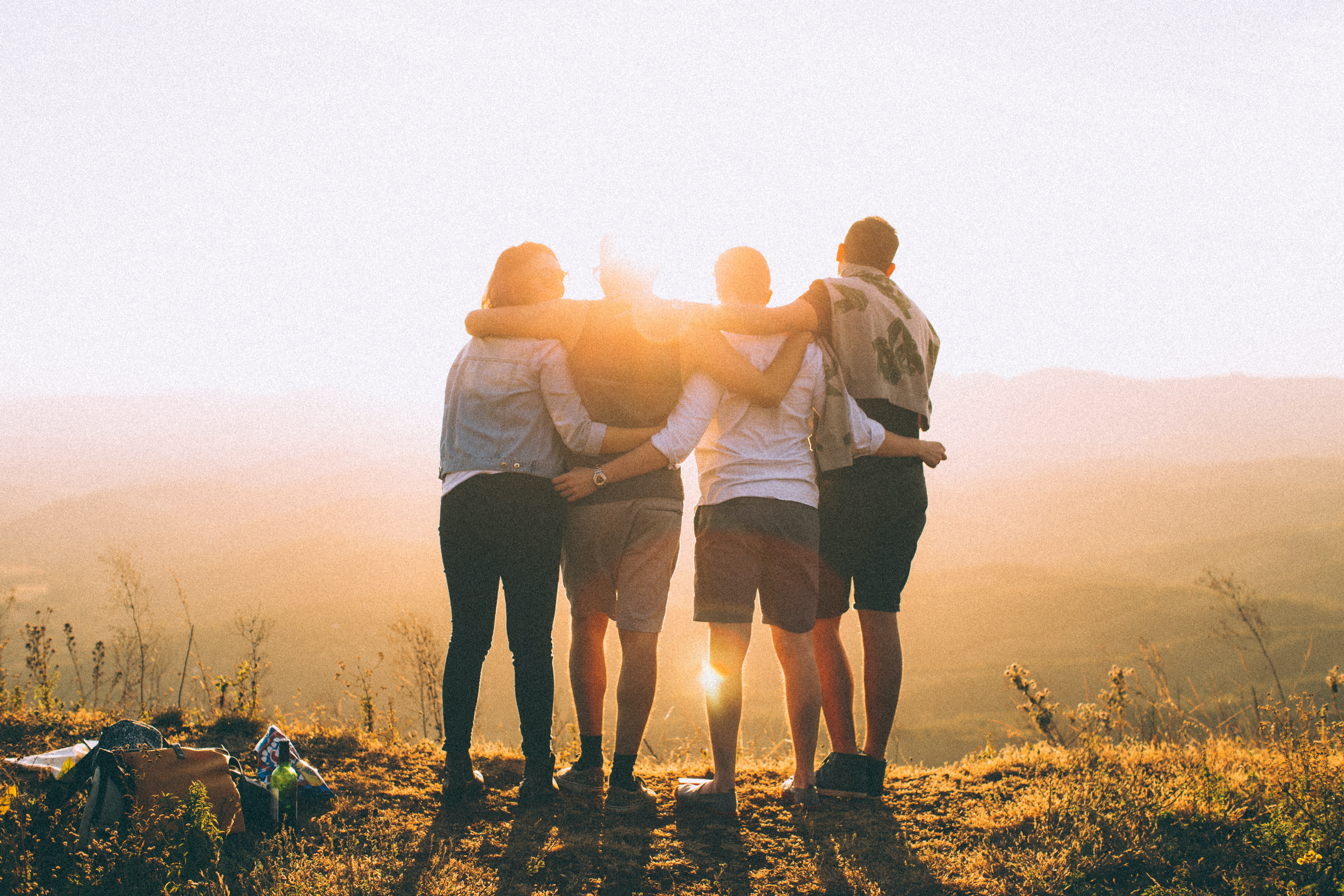 A group of people pictured from the back, they are hugging and watching the sunset.