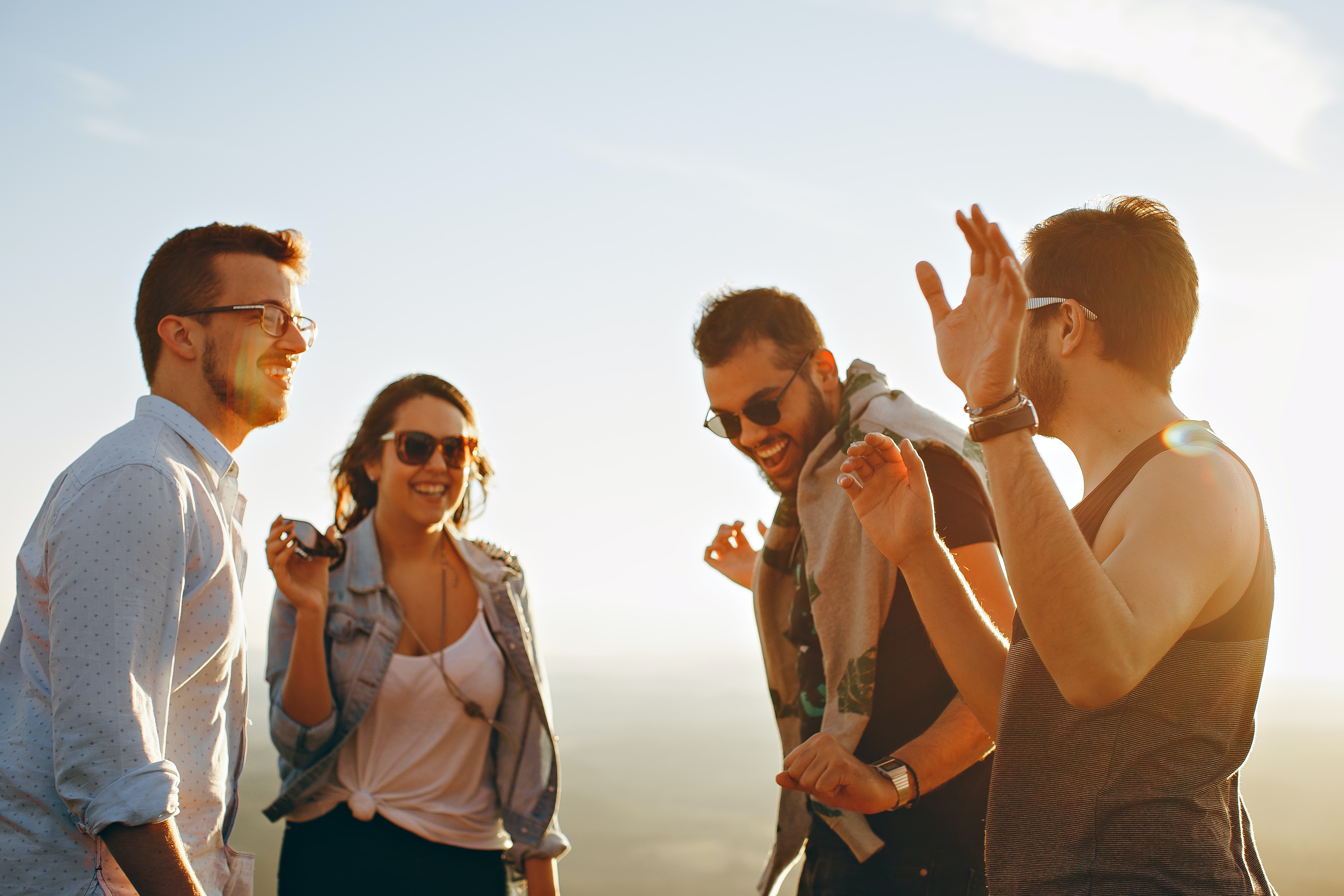 A group of people, all wearing sunglasses are laughing in the sun. 