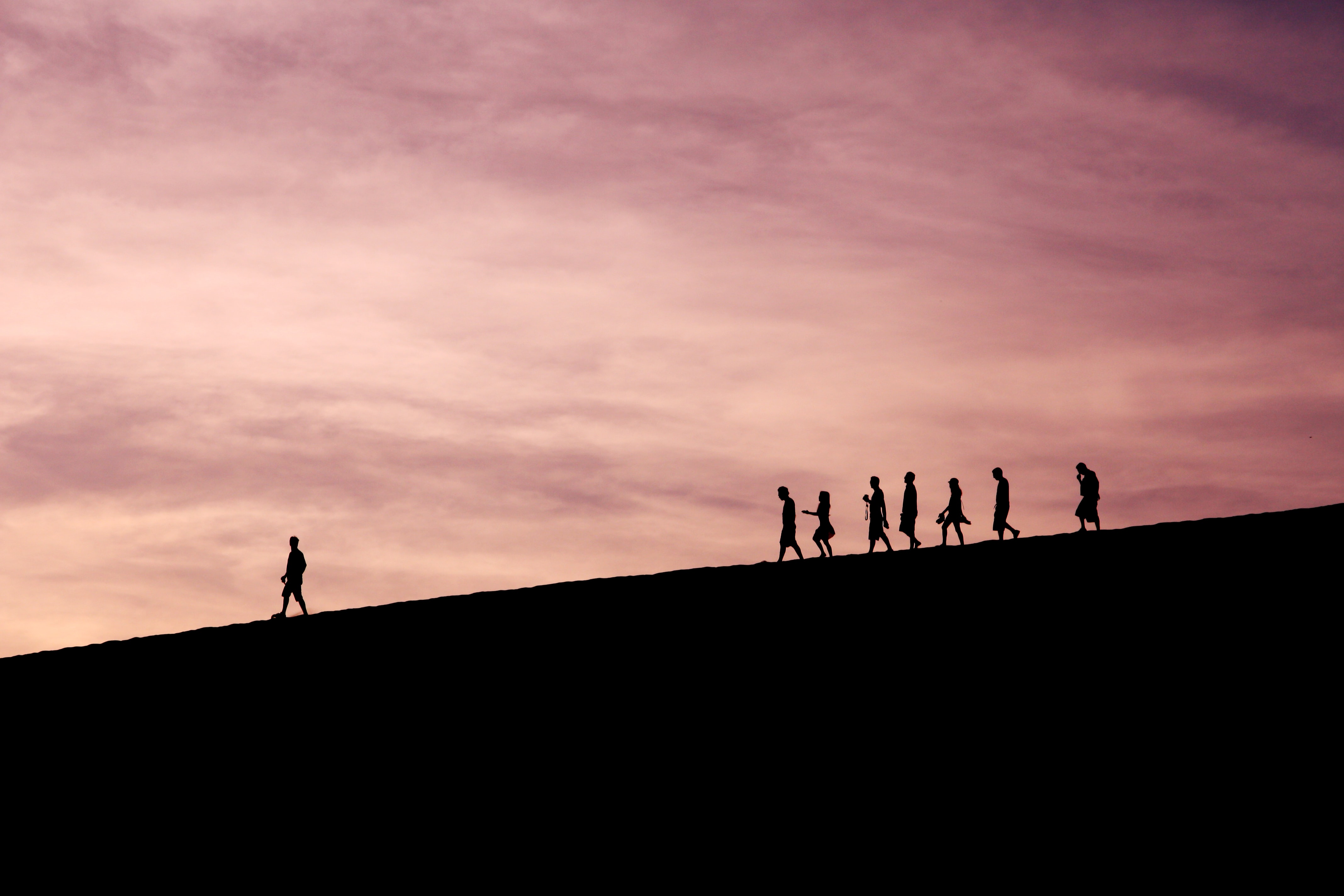 A group of people walking down a hill. One of them, the leader, is walking a little in front of them. 