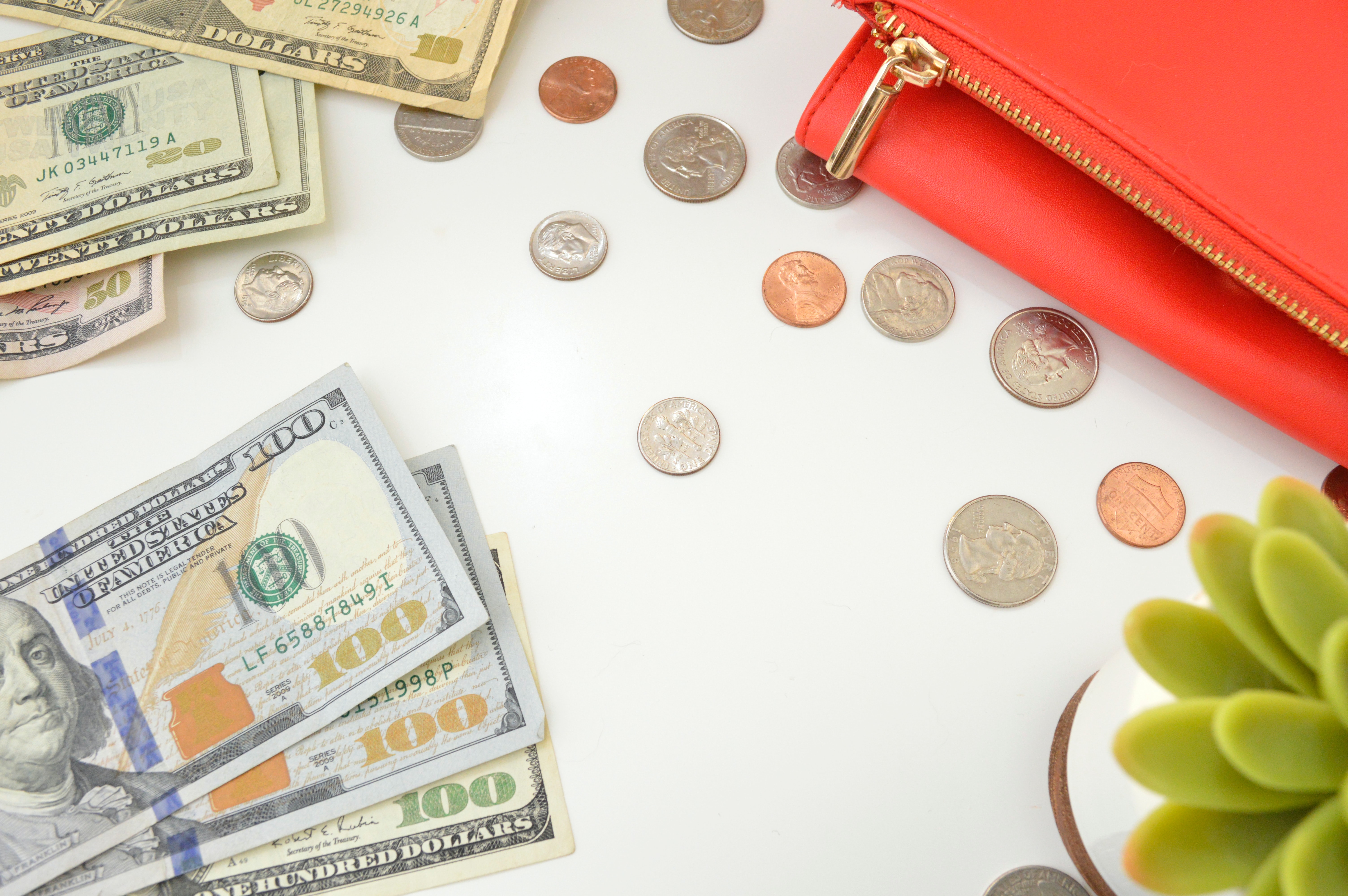 Money laid on top of a white table with a red wallet.