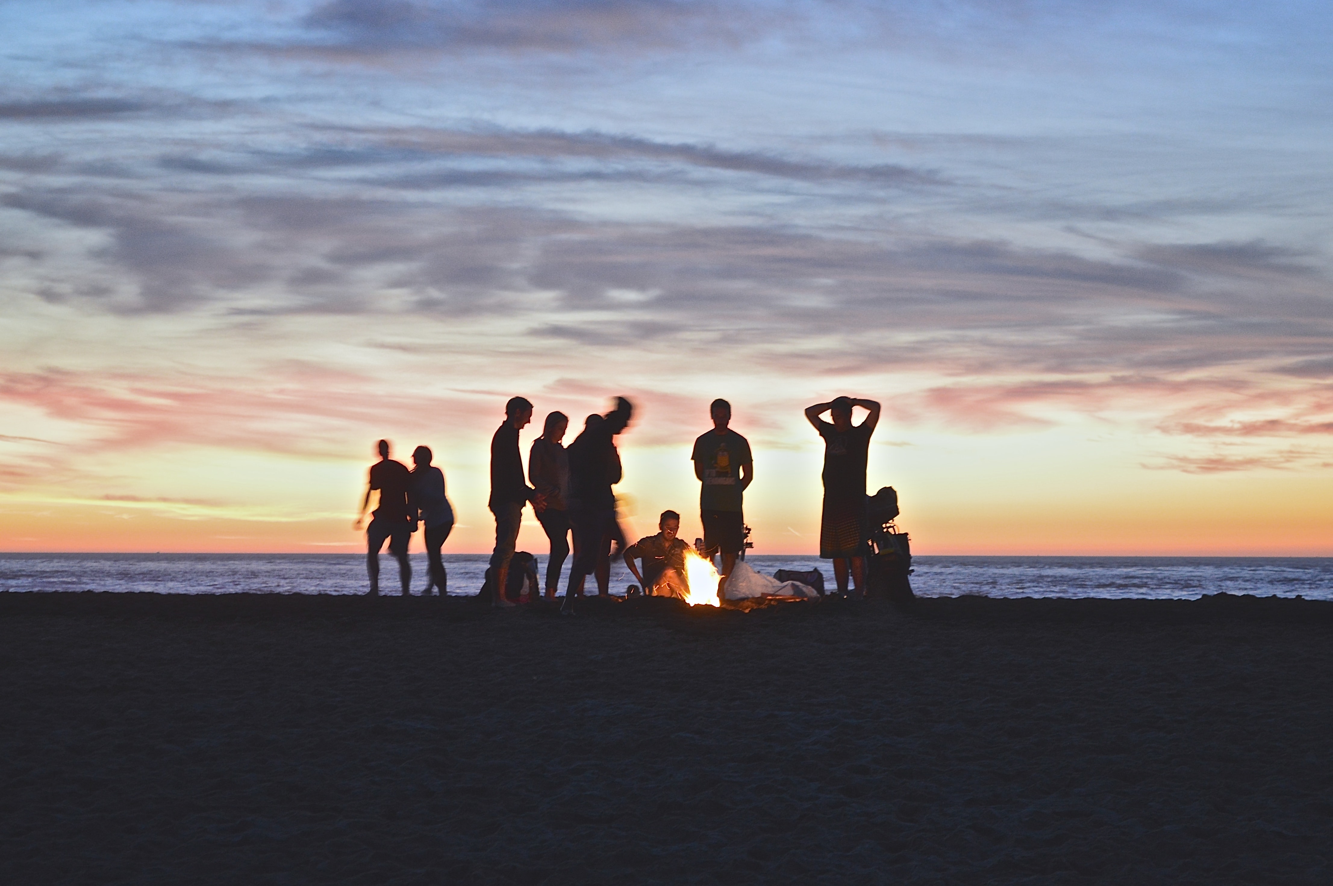 A group of people sitting around a bonfire at the beach.