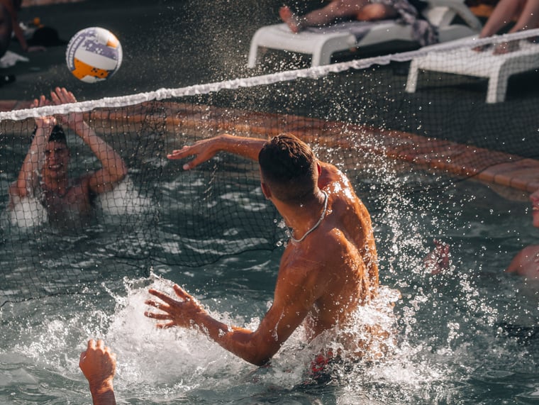 Two guys on a group trip playing volleyball in the pool.