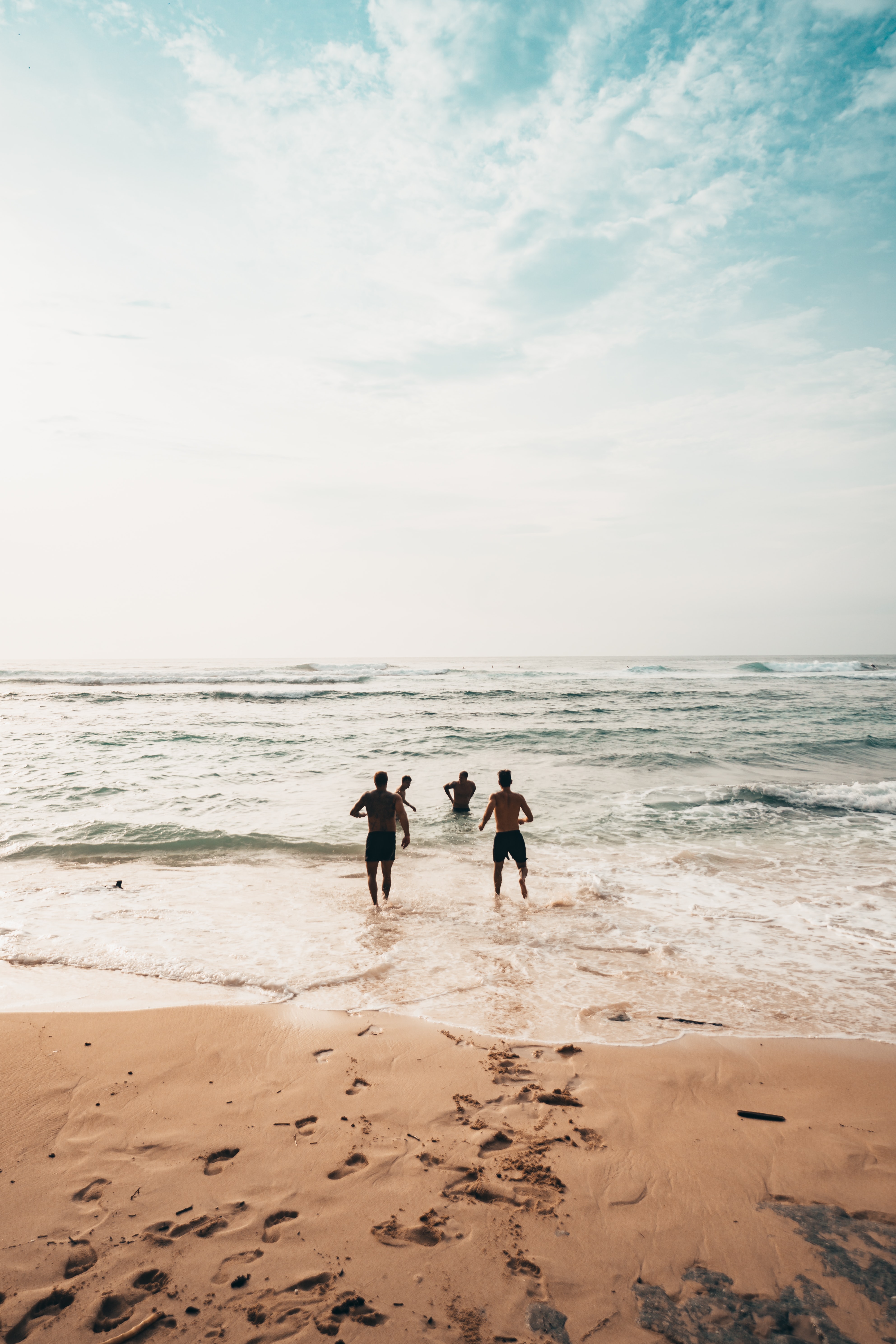 A group of friends run from a beach into the water.