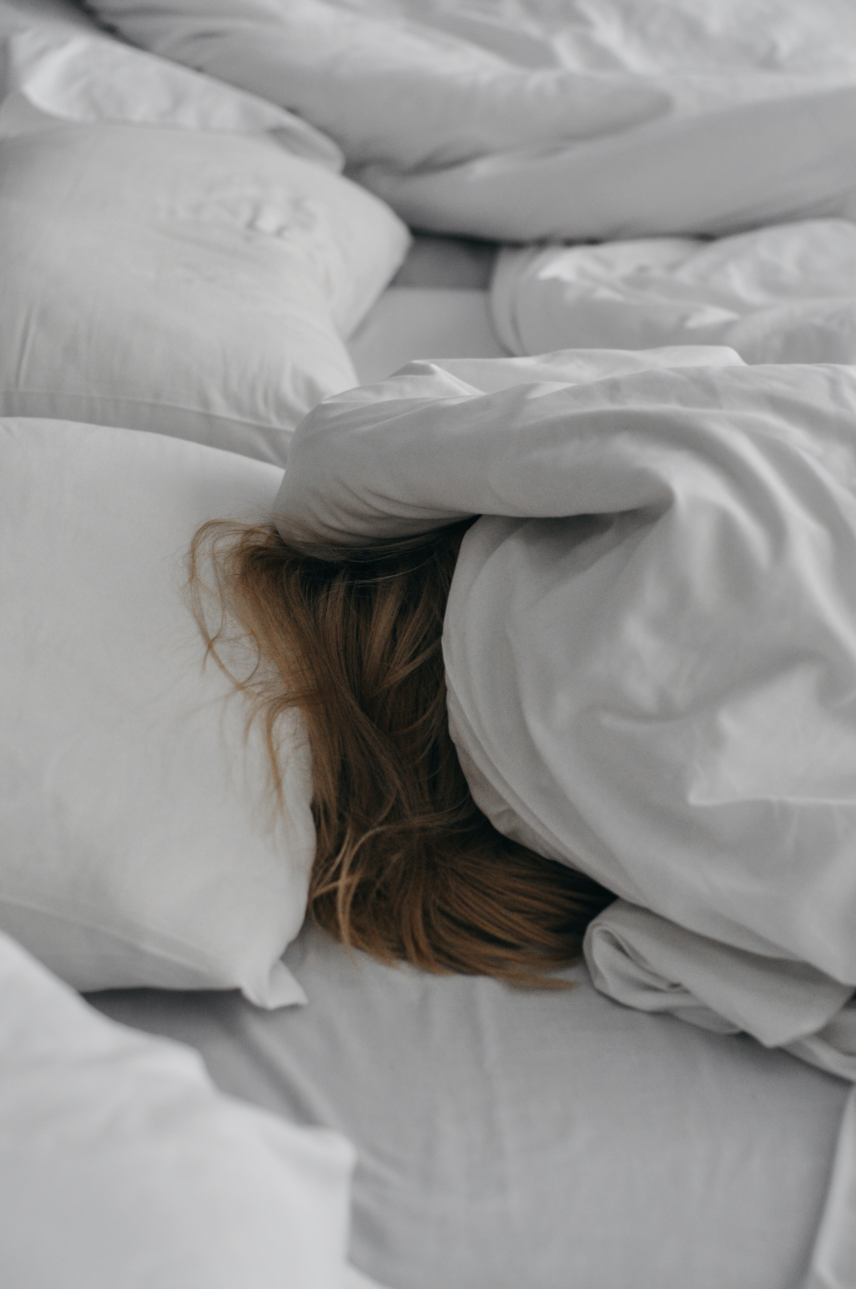 A blonde girl sleeping under white bed sheets.