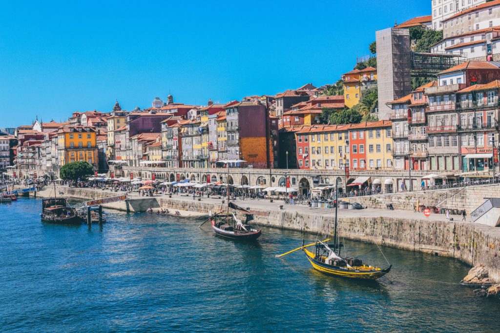 little boats on a river floating along side a city with colourful houses 