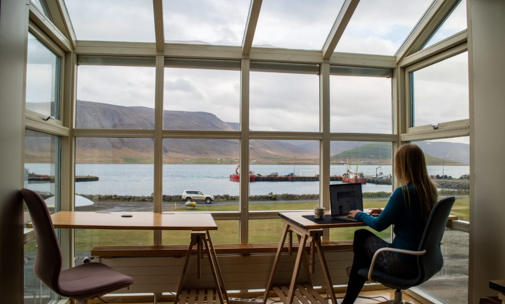 a woman sat with a laptop looking out on to a lake and mountain