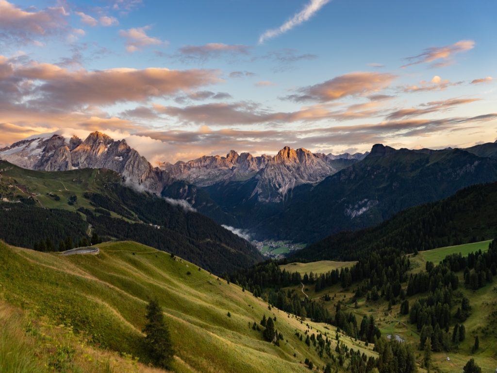 green grass fields and trees, surrounded by big mountains under white clouds and blue skies in Sella-Herbetet Traverse, Italy, the best hiking destination 