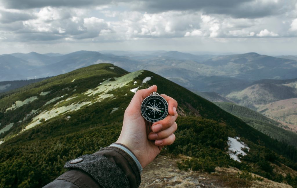 a hand holds up a compass with a view of mountains