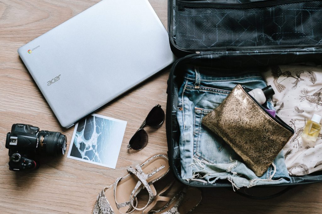 Open suitcase with a laptop, camera, sunglasses and clothes 