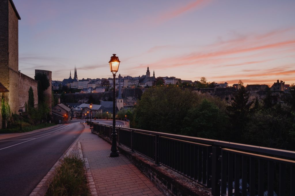 A purple sky over a street light on a bridge leading to a beautiful city