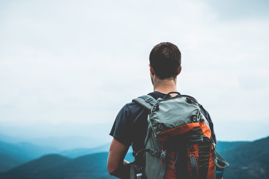 man standing looking over beautiful green landscapes with rucksack on 