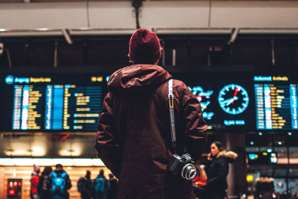 a man standing in front of the notice board in a train station a last minute travel tip