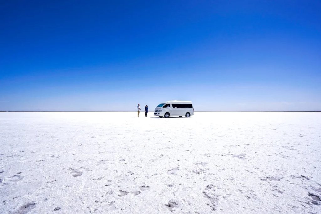 a white van and 2 people standing around in a white field of sand