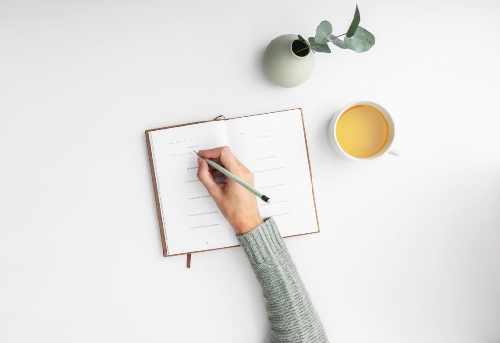 a diary being written inside with a cup of tea and plant next to it things to do during the coronavirus lockdown