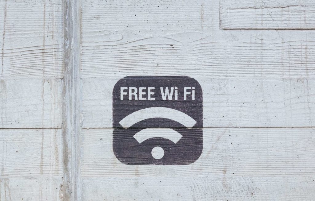 The words Free WiFi and the symbol of for WiFi on a dark grey square painted on a white wooden wall