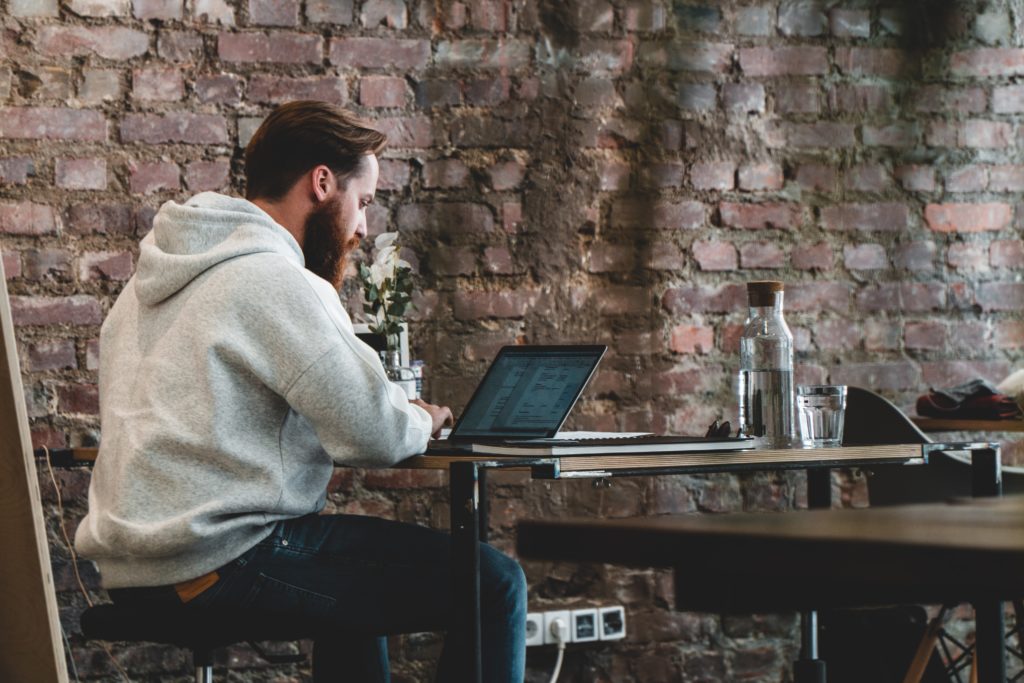 A man sitting on a desk working with a laptop infant of him reading travel news