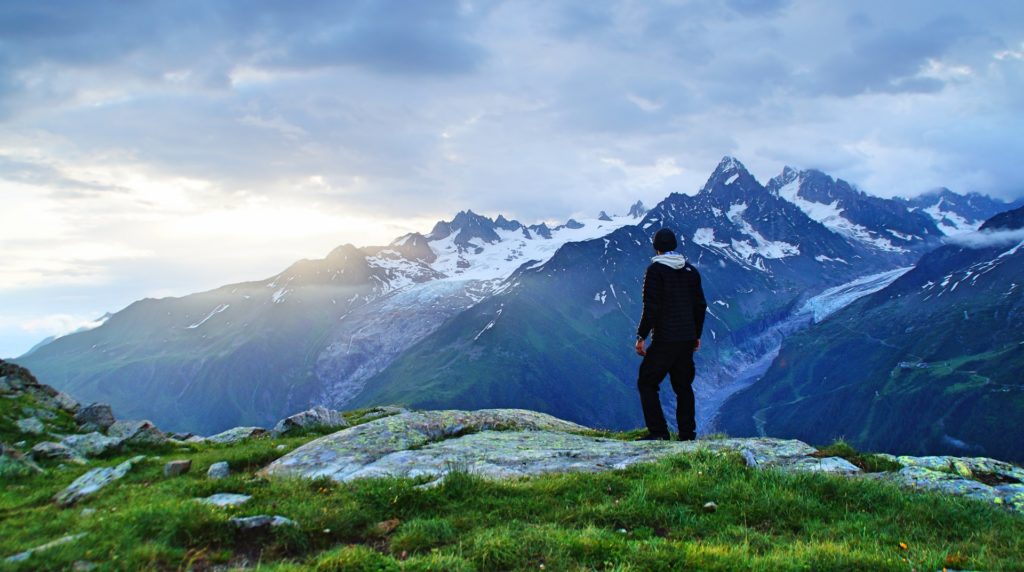 person standing on green grass while looking over a beautiful landscape in the french alps, the best hiking trail in Chamonix France