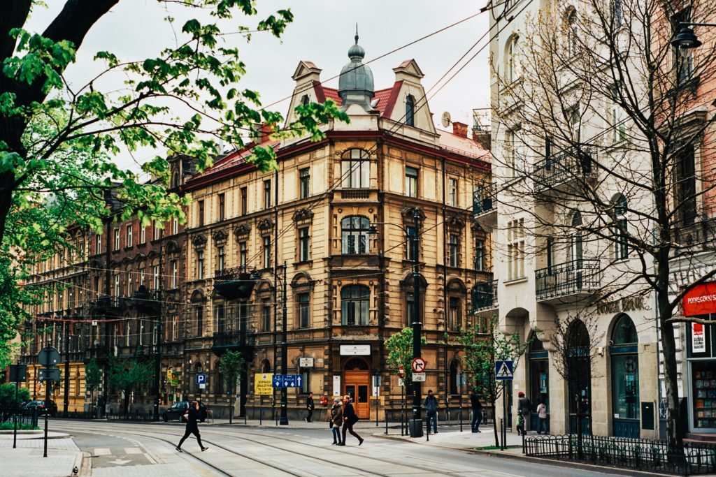 A beautiful old building right behind a green limb and people crossing an empty street in Krakow as one of the cheapest New Year destinations