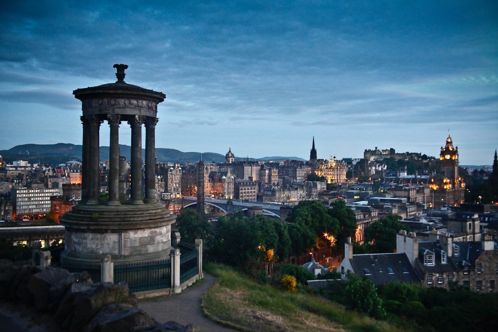 The city Endinburgh by evening with a small palace in the foreground and the city with all its lights in the background