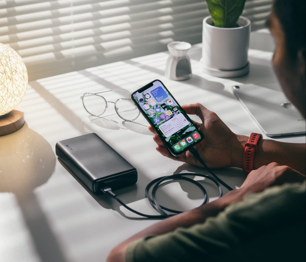 A man is holding a phone which is loading on a powerbank. 